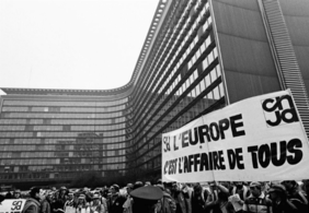 Schwarz-weiß Foto von Demonstrierenden, vor dem Gebäude der europäischen Kommission in Brüssel, ein Banner mit der Aufschrift "L'Europe c'est l'affaire de tous" ist zu sehen.